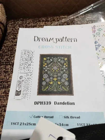 Buyer photo of the Dandelion kit packet showing the DPH339 sampler design on black fabric, with a chart page beside it